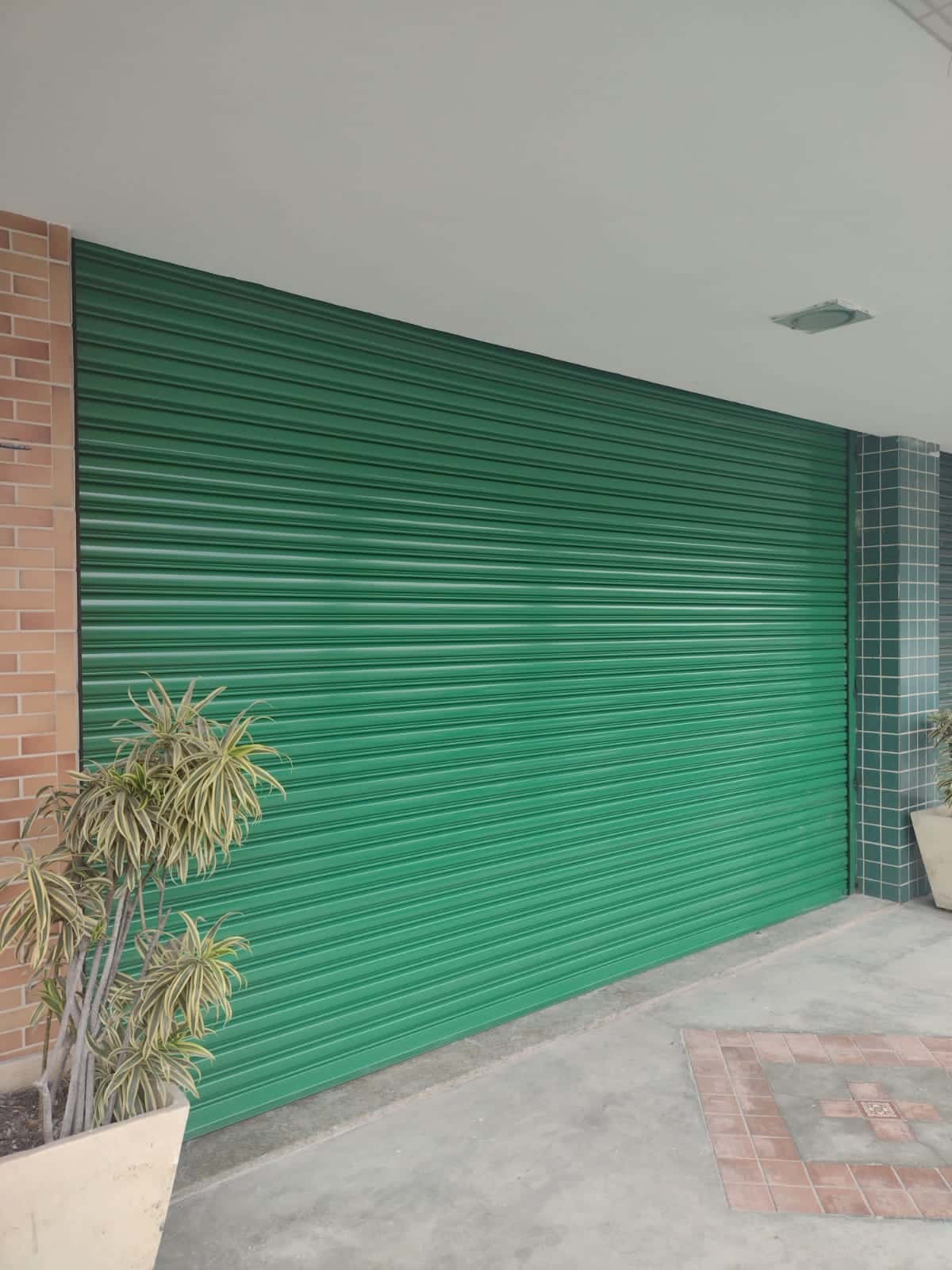 Porta de enrolar verde de grande vão em entrada de galpão