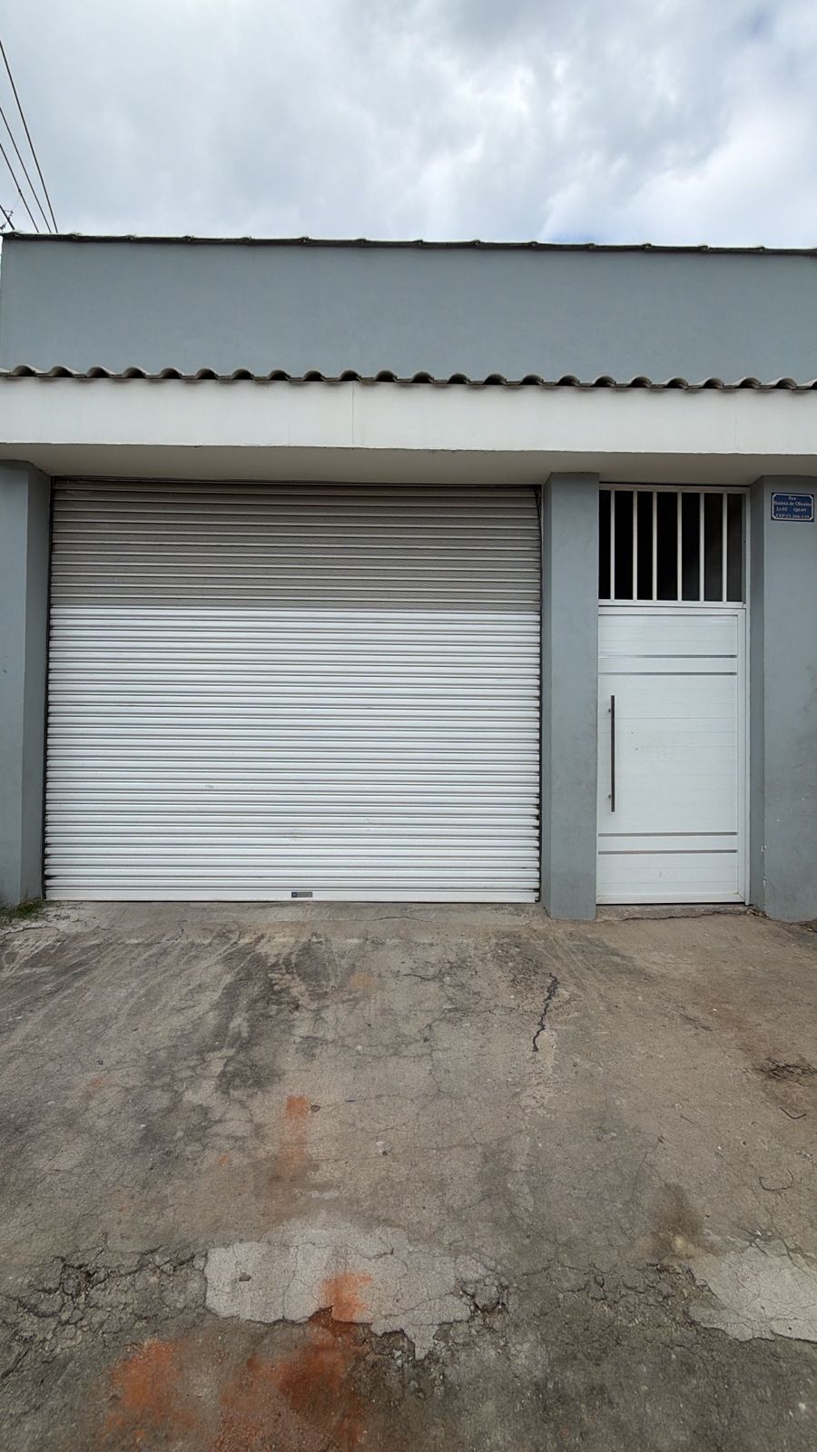 Porta de enrolar branca em garagem residencial com porta social ao lado